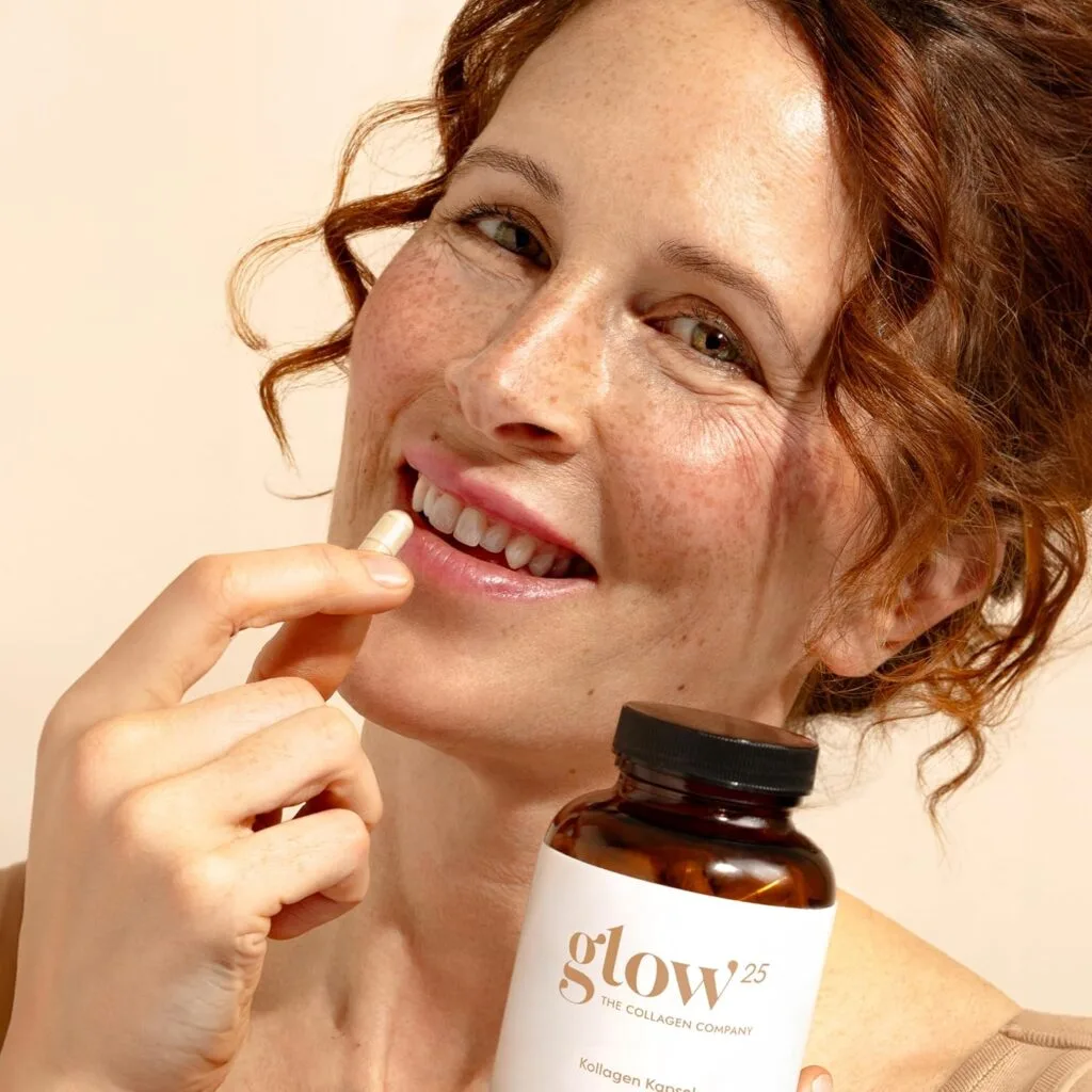 Une femme aux cheveux bouclés tient un flacon et une capsule de Glow25 - Collagen Complex Kollagen Kapseln mit Hyaluronsäure & Vitamin C, présentant les avantages du collagène, de l'acide hyaluronique et de la vitamine C pour une peau radieuse.
