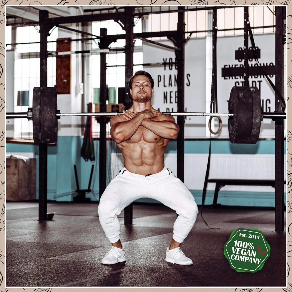 Un homme torse nu en pantalon blanc fait un squat avant avec un haltère dans une salle de sport ; le texte sur l'image indique "ProFuel - L-Arginin + L-Citrullin 6000 - 360 gélules vegan, 100% Vegan Company.