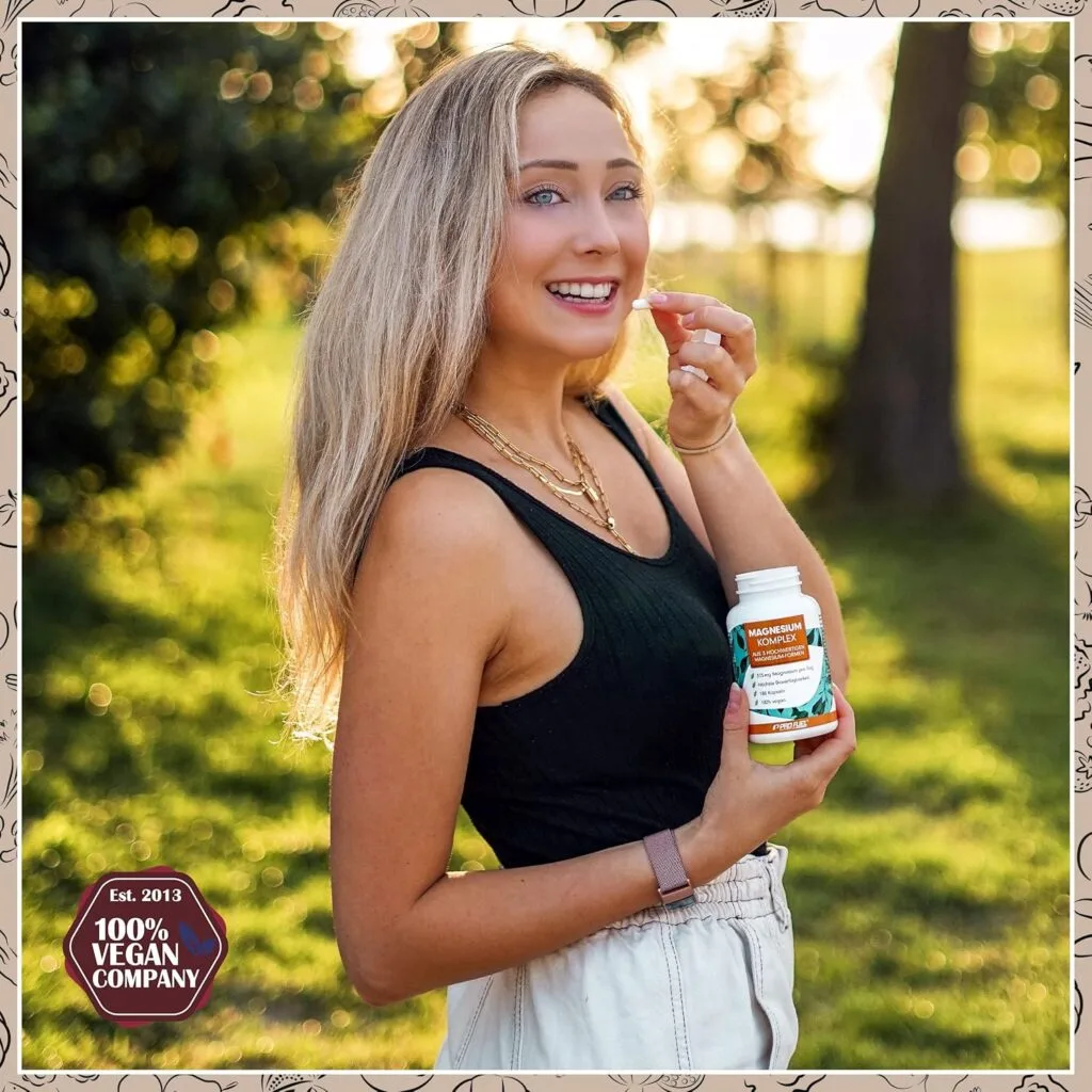 Une femme se tient à l'extérieur, souriant à l'appareil photo tout en tenant une bouteille étiquetée "Magnesium Complex ProFuel 400mg - Énergie & Récupération 180 Gélules" dans une main et une capsule dans l'autre. Le texte indique "100% Vegan Company.