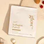 Un paquet blanc étiqueté "Glow25® Collagène en poudre [450g]" avec un texte doré repose sur une surface beige à côté d'une cuillère, de framboises et d'un petit bol - idéal pour tous ceux qui recherchent du collagène hydrolysé ou de la protéine Maroc dans leur routine quotidienne.